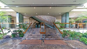 Un moderno vestíbulo de hotel con una escalera central, plantas en macetas y vista al interior.