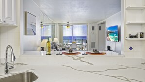 A modern kitchen with a large island, a built-in sink, and a view of the ocean through large windows. - Ocean-Marina Yacht Views Condo Steps to the Beach w/Full Kitchen & Free WiFi (Honolulu)
