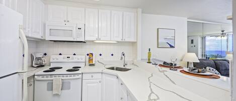 A modern kitchen with white cabinetry, a built-in microwave, a stove, and a large island with a sink.