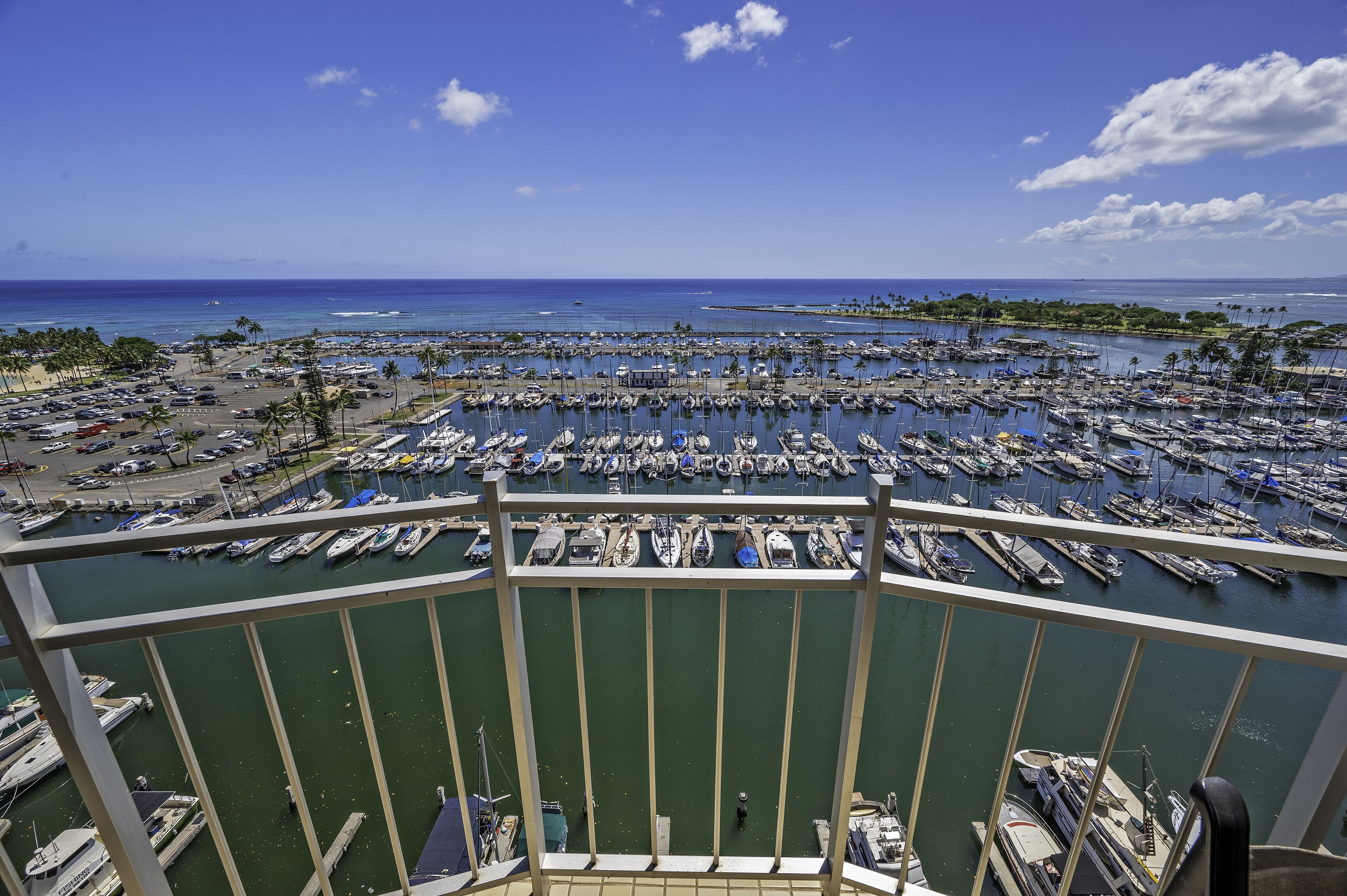 A marina with numerous boats docked, a clear blue sky, and a view of the ocean.