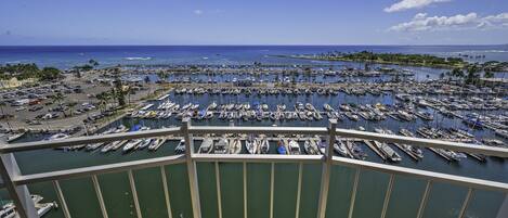 A marina with numerous boats docked, a clear blue sky, and a view of the ocean.