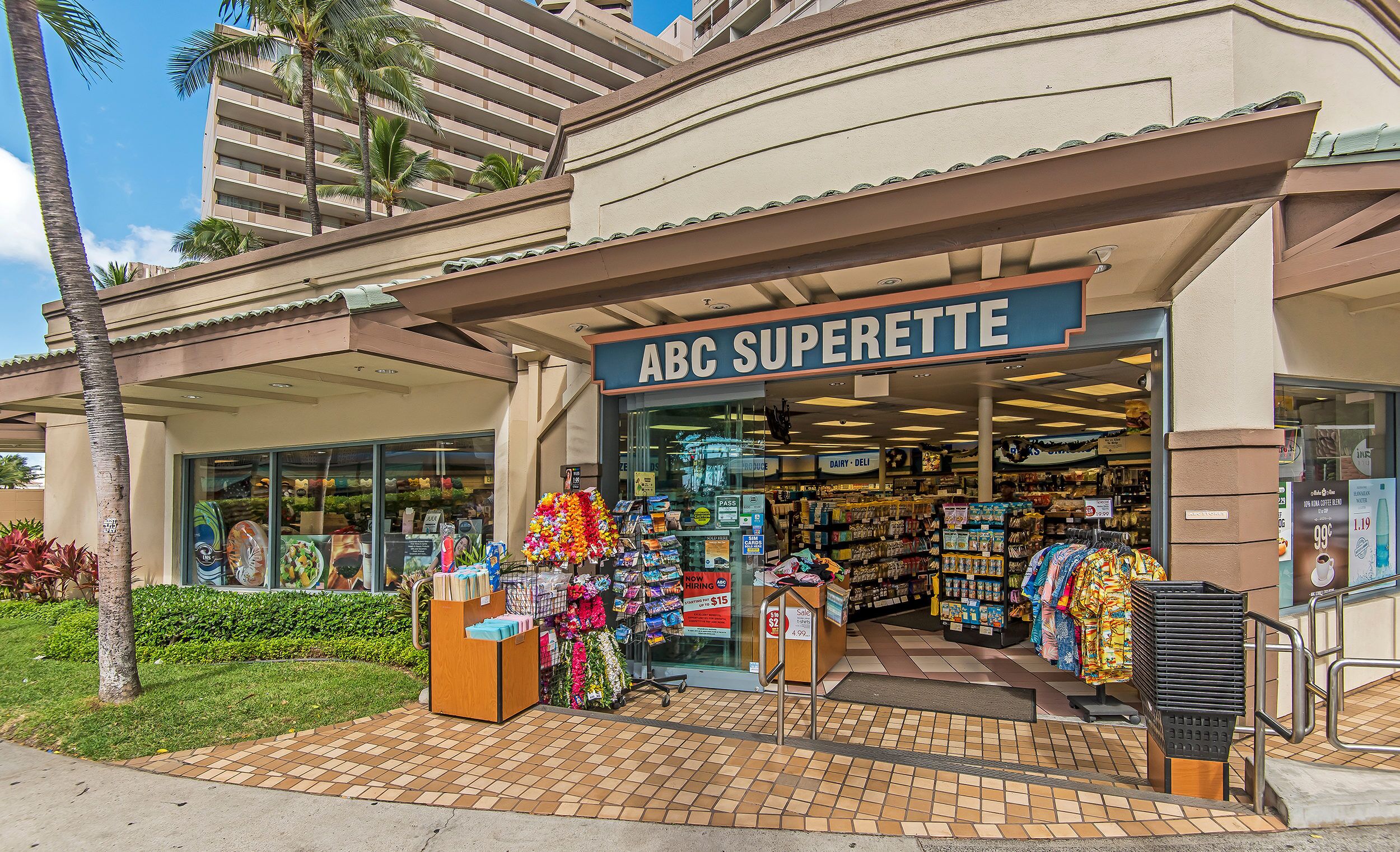 L’extérieur de l’épicerie ABC Superette se distingue par son entrée carrelée, une vitrine présentant une variété de produits colorés et une vue dégagée sur l’intérieur du magasin.