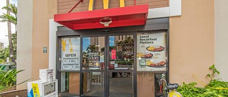 A McDonald's restaurant with a red awning, glass doors, and a bicycle parked outside.