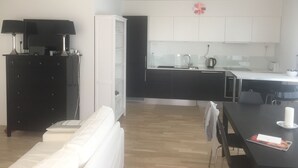 Ett modernt kök med vita skåp, en svart bänkskiva och en matplats med ett vitt bord och stolar.