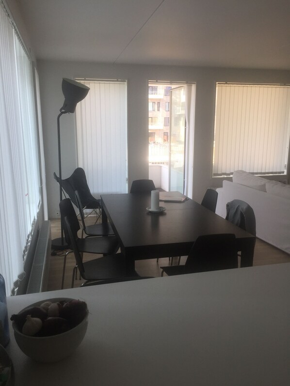 A modern living room with a dining area, featuring a large table, black chairs, a floor lamp, and a sofa. - Islands Brygge (København)