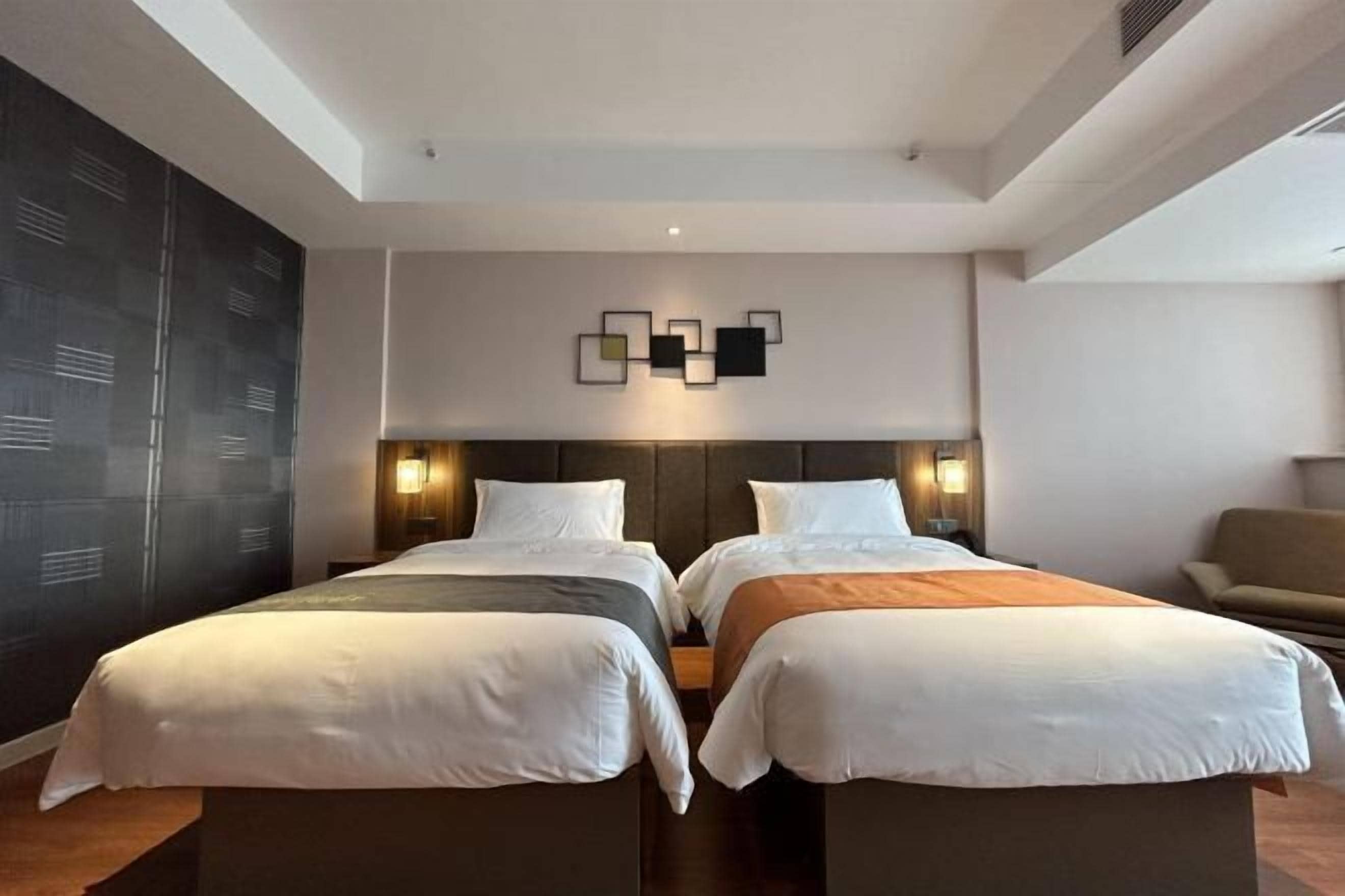 Habitación de hotel con dos camas, una pared oscura con un diseño geométrico y una lámpara moderna sobre las camas.