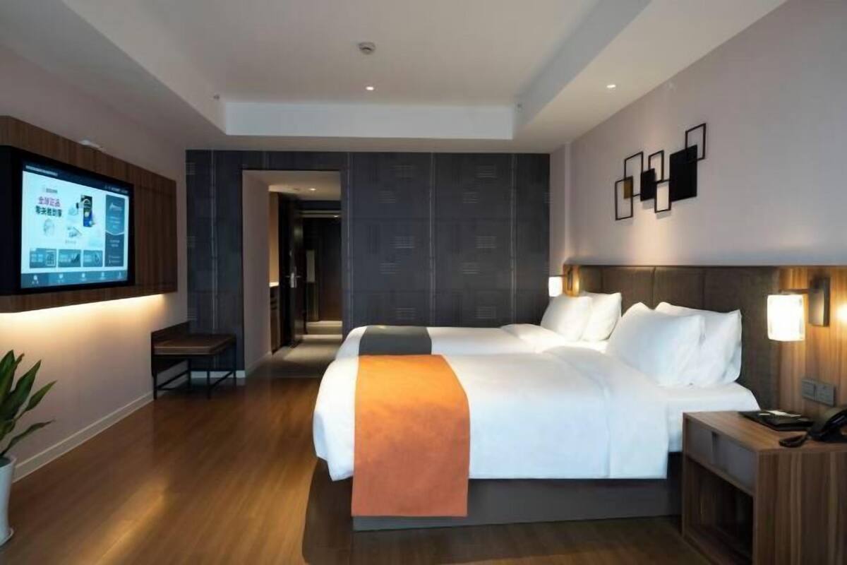 Une chambre d’hôtel moderne avec un grand lit, un téléviseur fixé au mur et un bureau avec une lampe.