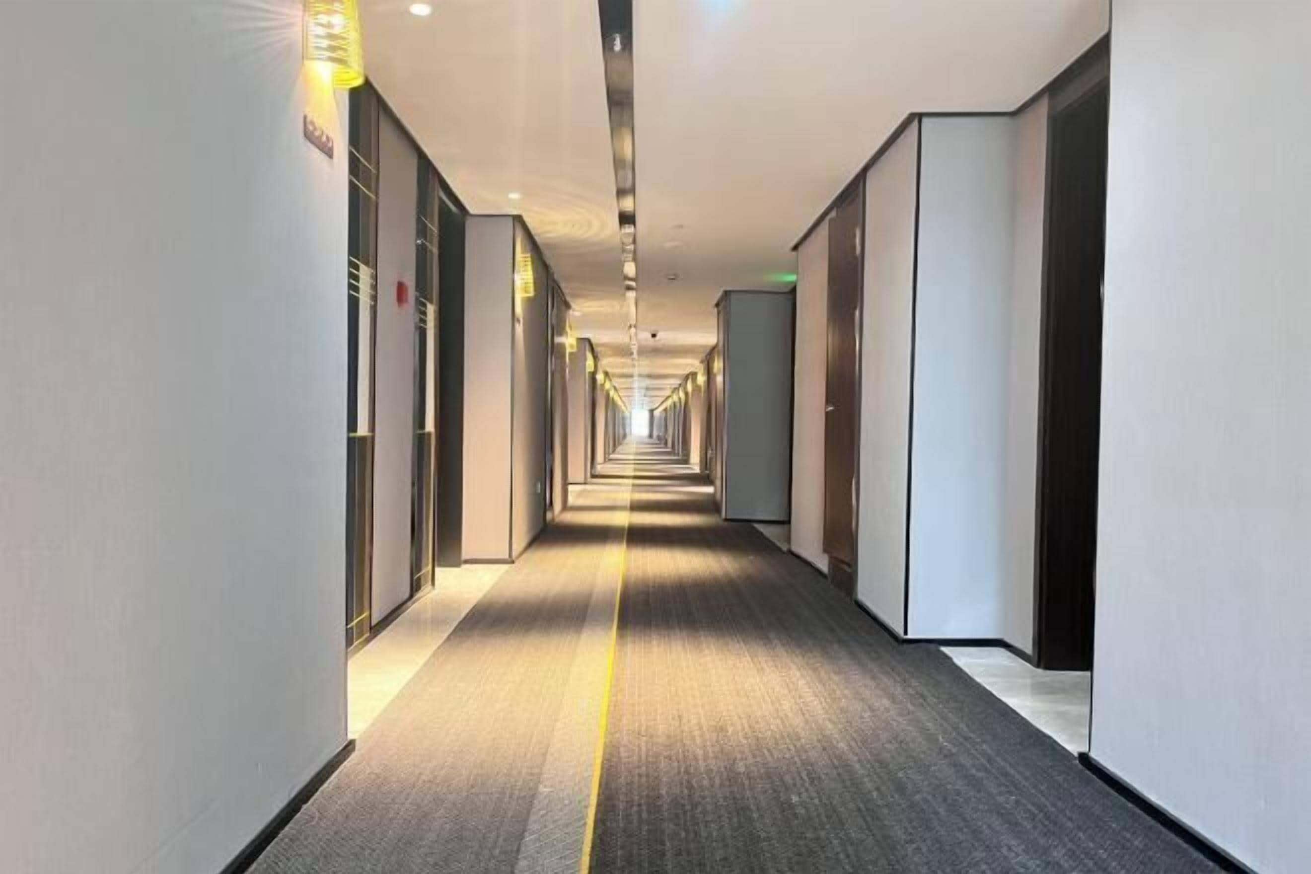 A long, narrow hotel corridor with a carpeted floor and doors on both sides.