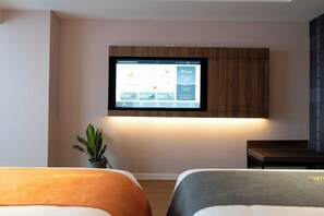 Habitación de hotel con cama, una mesita, una planta en maceta y un televisor de pared mostrando una aplicación del hotel.
