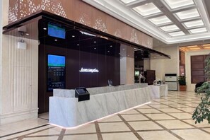 A hotel reception area with a marble counter, digital display, and a large screen.