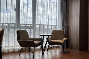 Habitación con dos sillas, una mesita pequeña, ventanas amplias con vistas y suelo de madera.