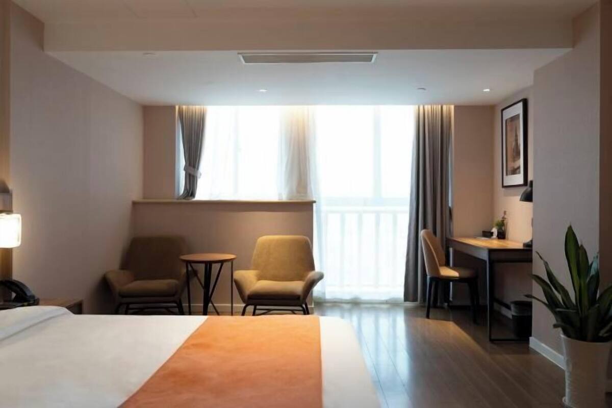 Une chambre d’hôtel avec un lit, deux fauteuils, un bureau et une plante en pot.