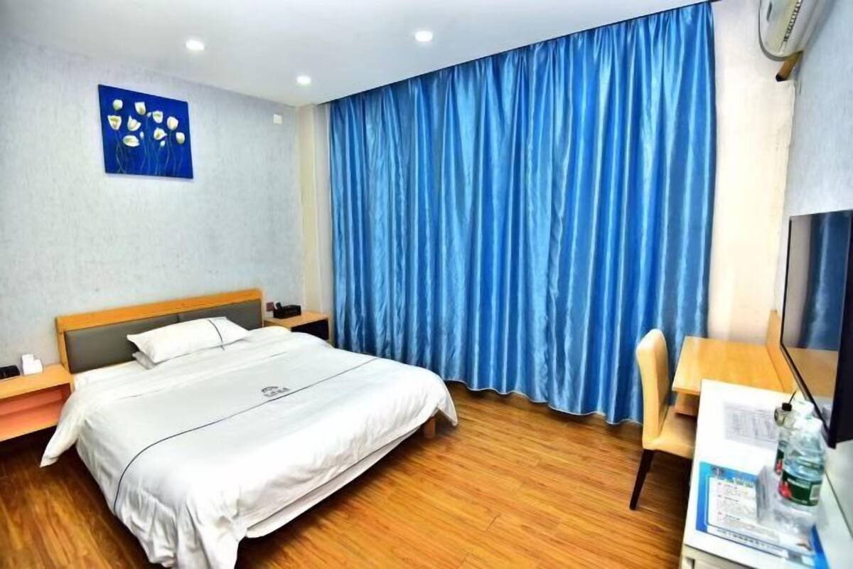 Een hotelkamer met een bed, een bureau, een stoel, een blauw gordijn en een kunstwerk aan de muur.