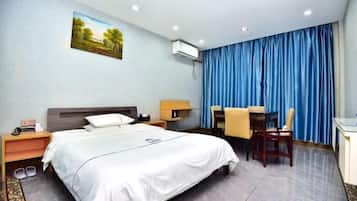 A hotel room with a bed, a desk, a chair, a nightstand, and a wall-mounted air conditioner.