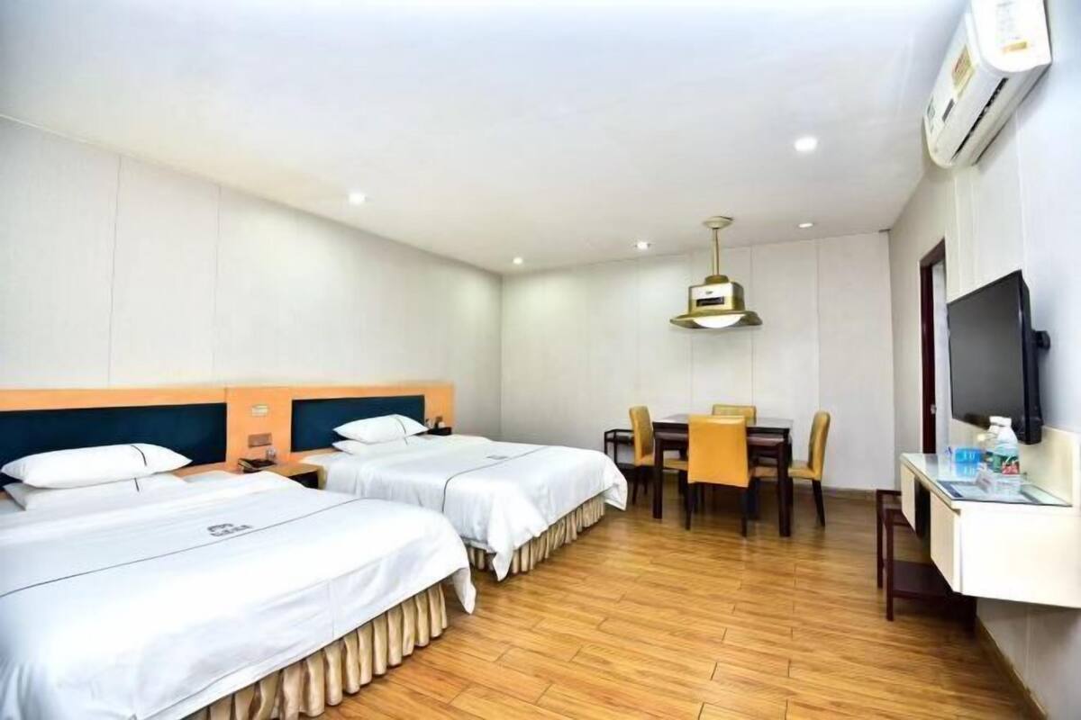 Een hotelkamer met twee bedden, een eettafel met stoelen, een televisie en een airconditioning.