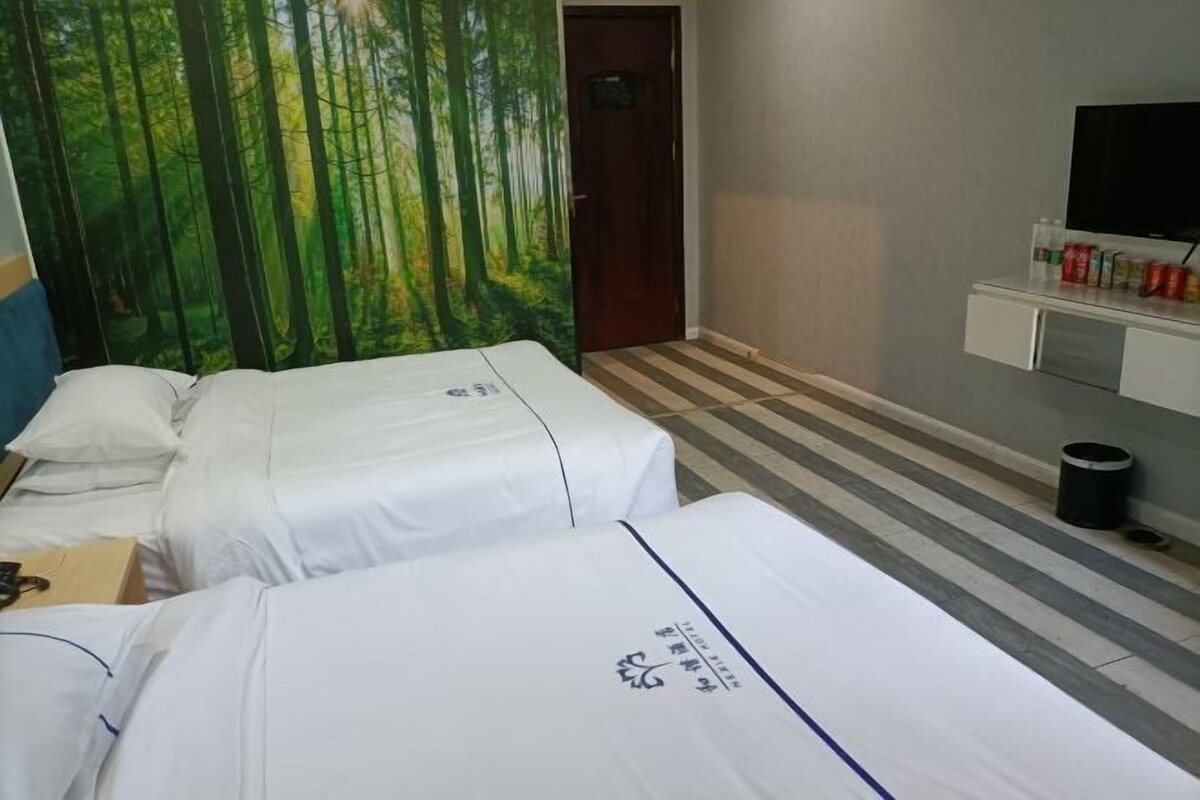 A hotel room with two beds, a television on a stand, and a painting of a forest on the wall.