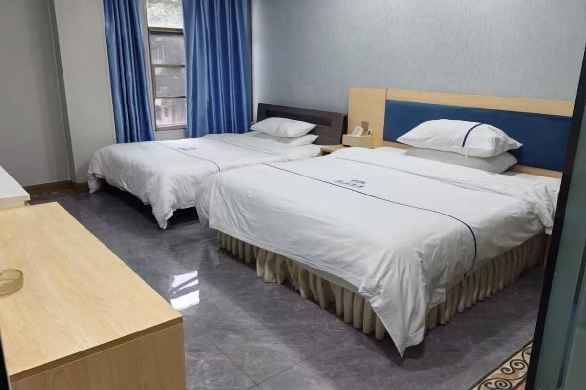Een hotelkamer met twee bedden, een houten bureau en een raam met gordijnen.