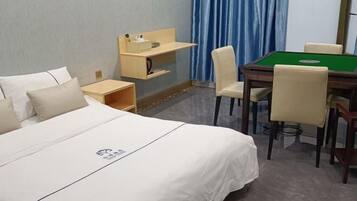 A hotel room with a bed, a desk with a chair, a green pool table, and a blue curtain.