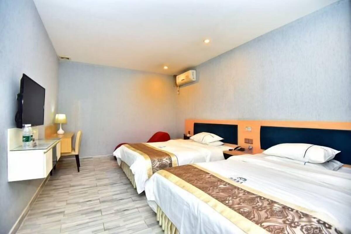 Een hotelkamer met twee bedden, een bureau, een stoel, een televisie en een airconditioning.