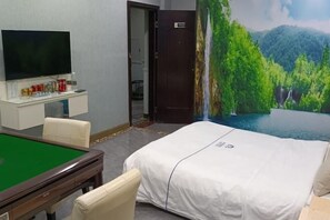 A hotel room with a green pool table, a bed with a white bedspread, a television on a stand, and a mural of a forest waterfall. - He Xie Hotel (Zhuhai)
