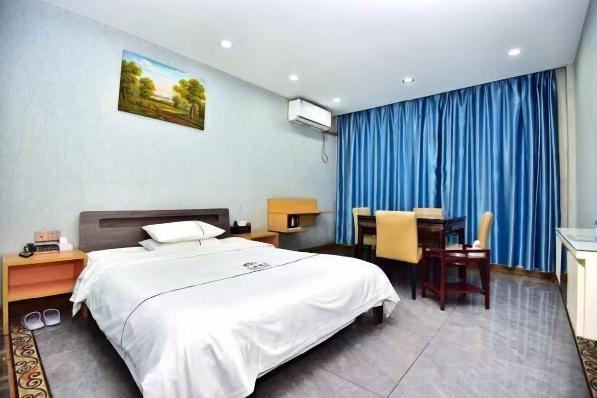 Een hotelkamer met een bed, een bureau, een stoel, een lamp en een schilderij aan de muur.