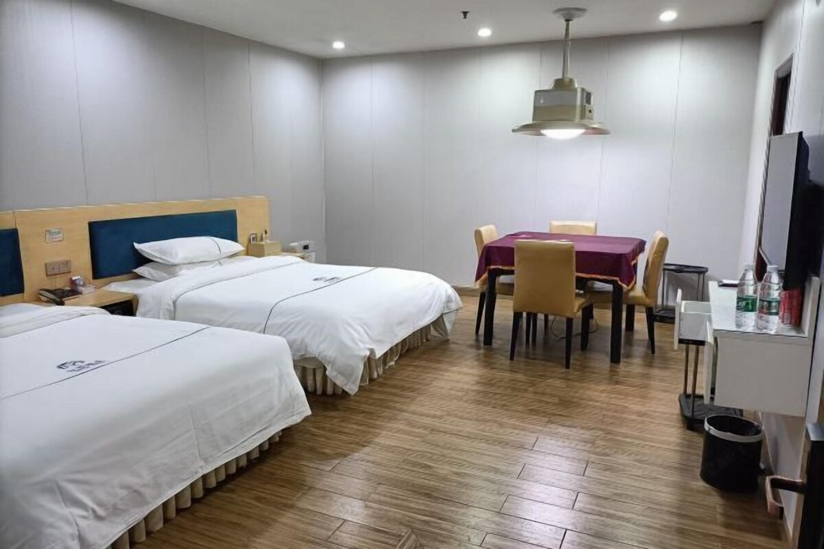 A hotel room with two beds, a dining table with chairs, a TV, and a trash bin.