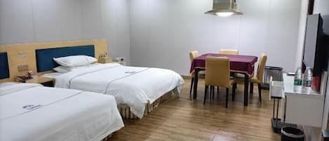 A hotel room with two beds, a dining table with chairs, a TV, and a trash bin.