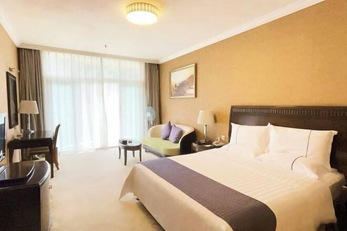 A hotel room with a large bed, a desk, a chair, a small table, and a sofa.