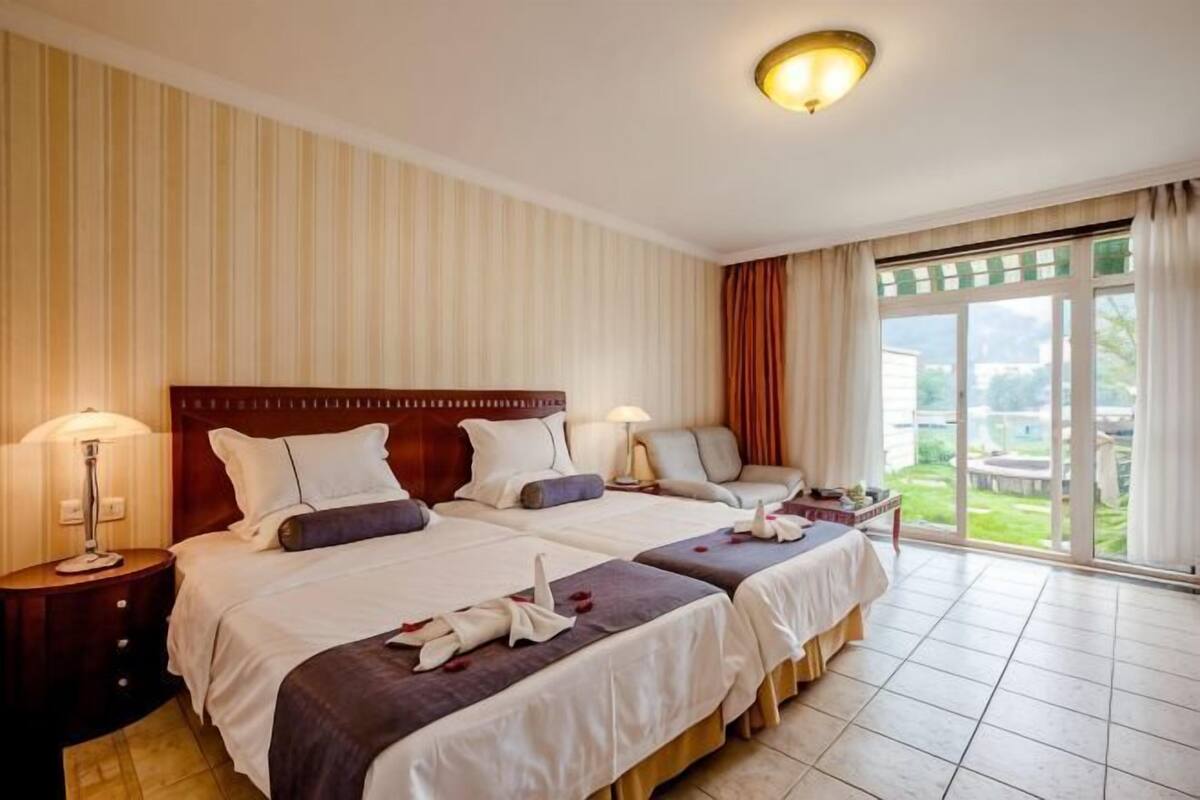 A hotel room with two beds, a large window, and a view of the outdoors.