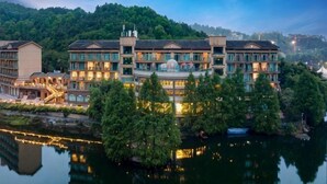 A multi-story hotel with a reflection in the water, surrounded by trees and a hilly backdrop. - Sky & Sea Resort (Chongqing)