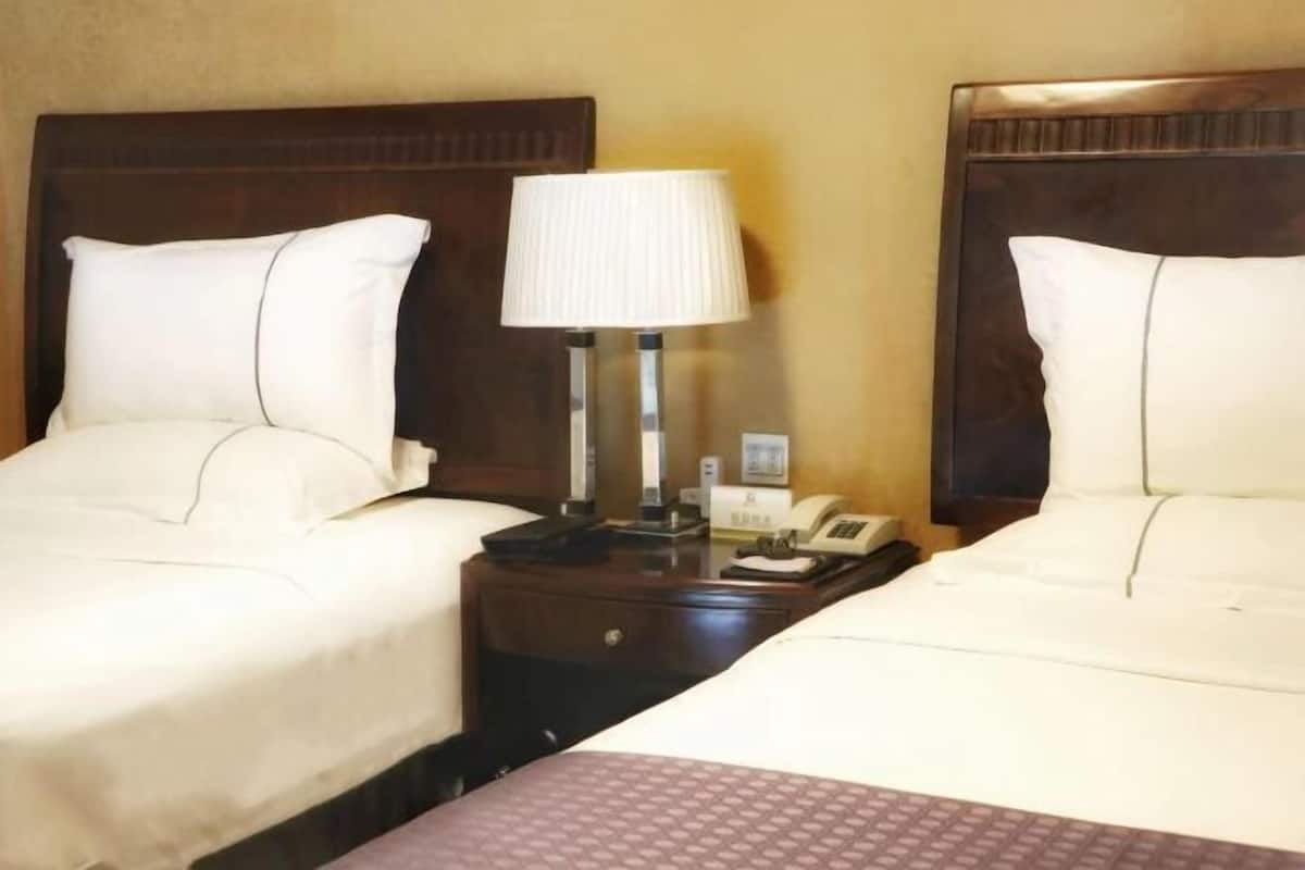 A hotel room with two beds, each with white linens, a bedside table with a lamp, and a telephone.
