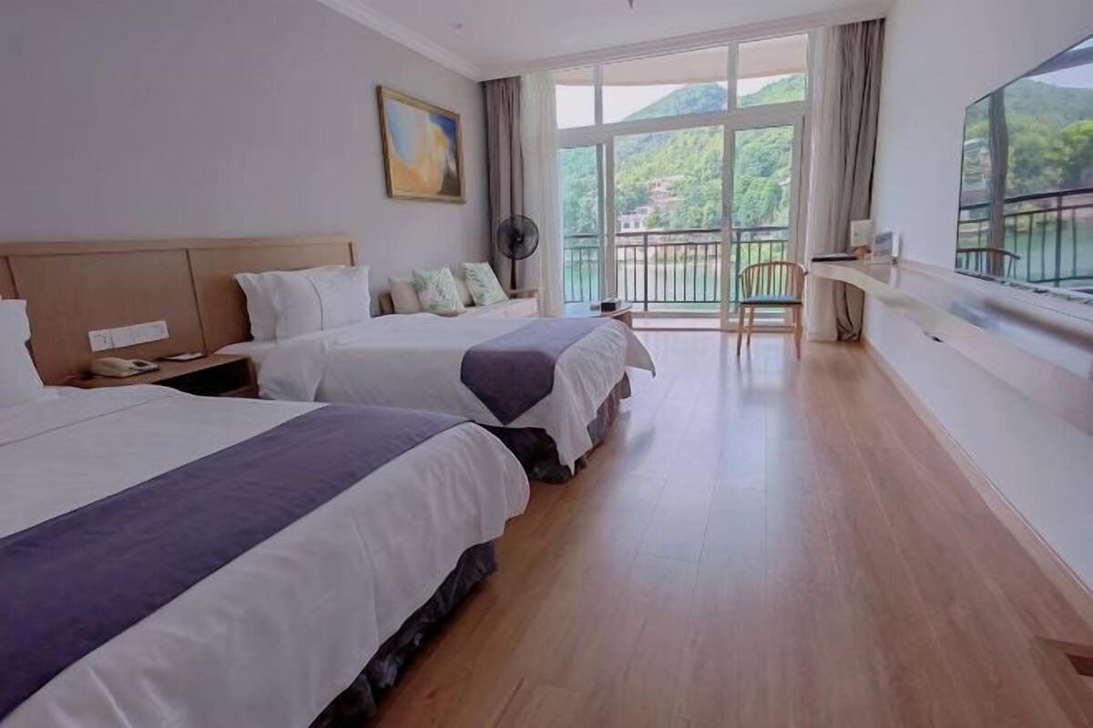 A hotel room with two beds, a balcony, and a large window offering a view of greenery.