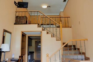 A staircase with a wooden handrail and metal balusters, leading to a landing with a flat ceiling and a television mounted above. - Sky Sea Resort (Chongqing)