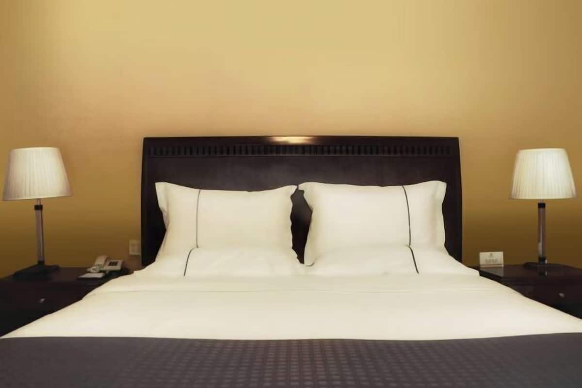 A hotel room with a large bed, two bedside lamps, and a dark headboard.