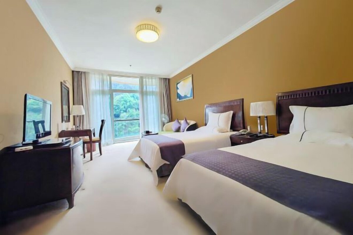 A hotel room with two beds, a desk with a television, a chair, and a window with a view.