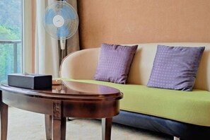A room with a sofa, a table, and a standing fan. - Sky Sea Resort (Chongqing)