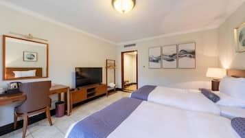 A hotel room with two beds, a desk with a television, a chair, and artwork on the walls.