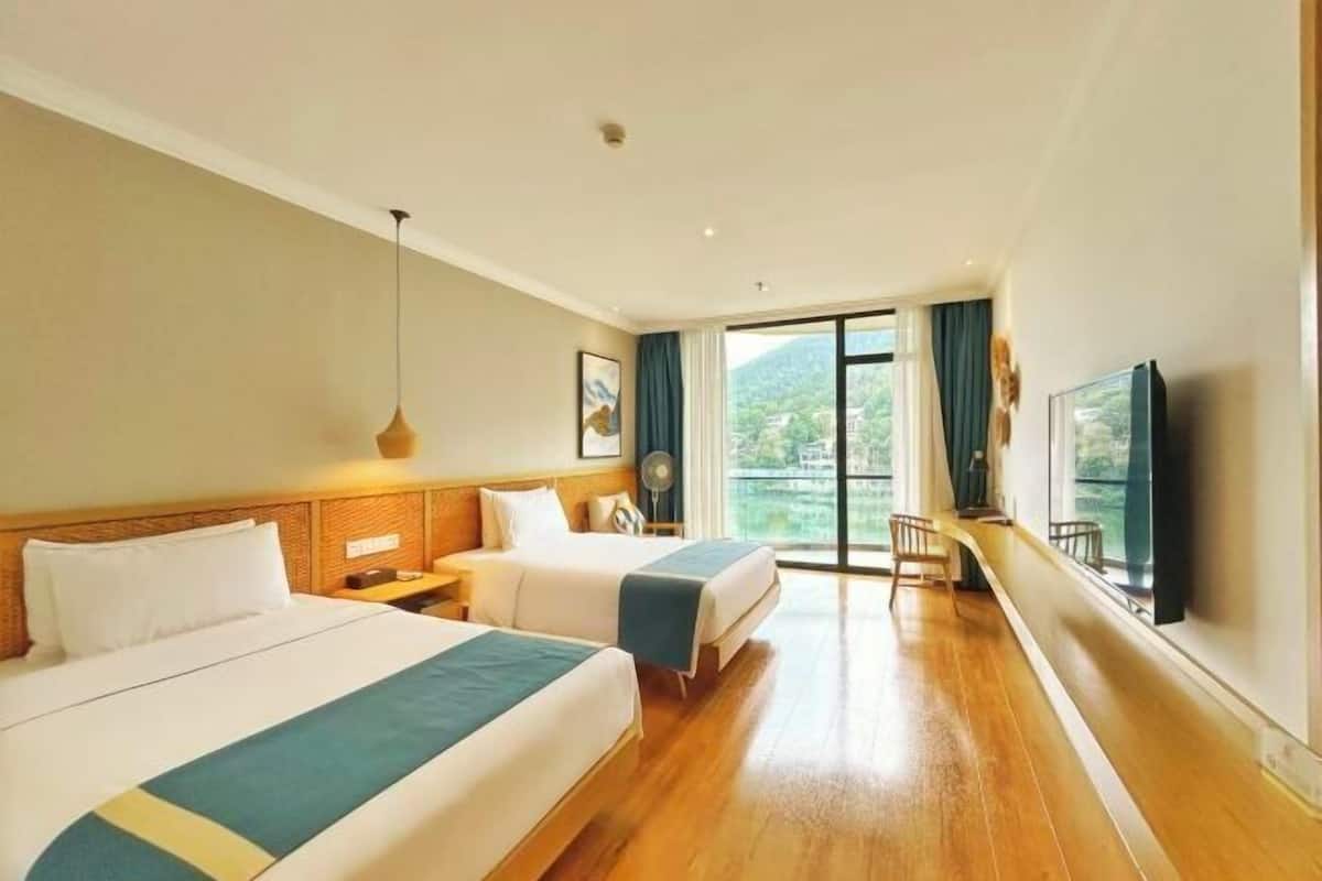 A hotel room with two beds, a TV, a balcony with a view, and a wooden floor.