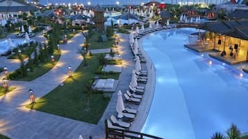 A resort with a large swimming pool, lounge chairs, and a well-lit walkway.