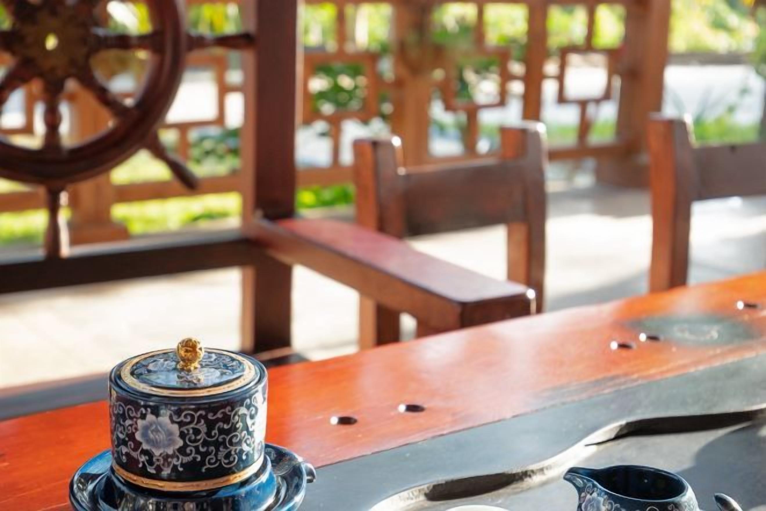 A wooden table with a decorative tea set, including a teapot and cups, and a wooden chair in the background.