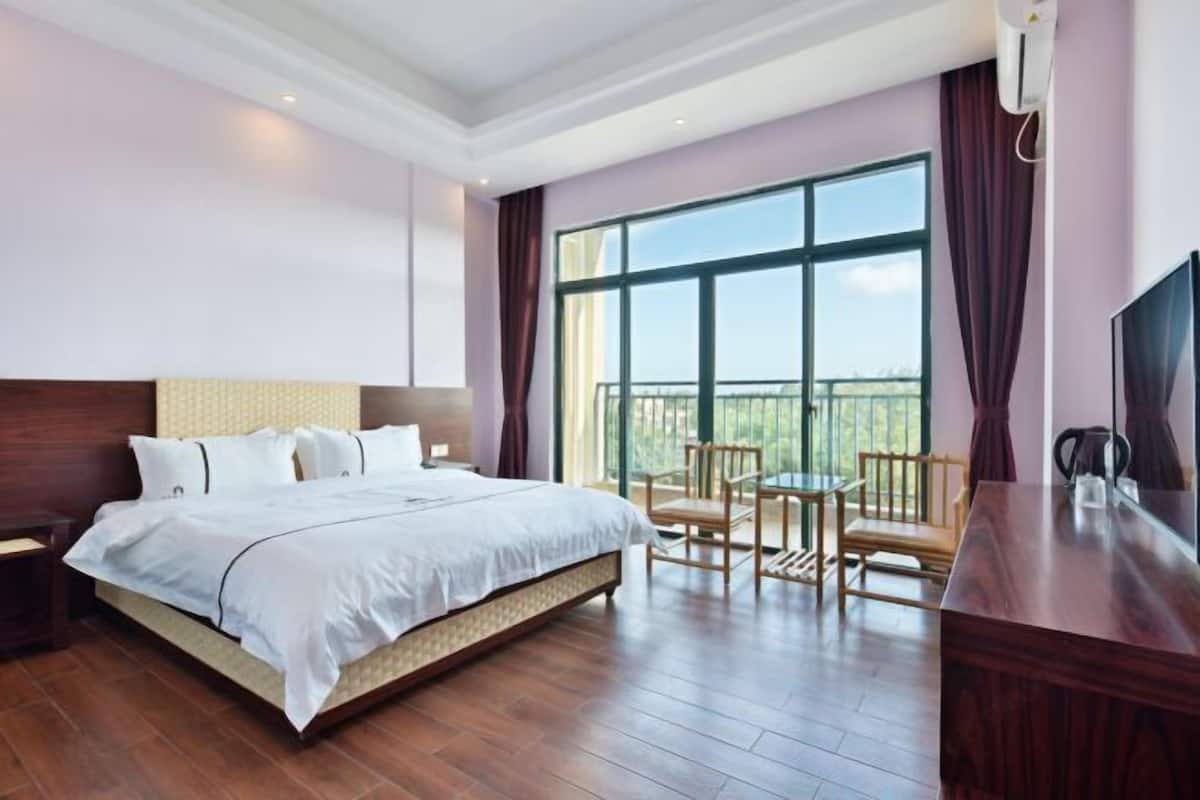 Ein Hotelzimmer mit einem großen Bett, einem Fernseher, einem Balkon mit Sitzgelegenheiten und einem Holztisch.