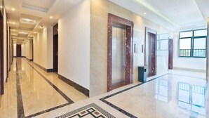 A spacious hotel corridor with a marble floor, a large mirror, and a modern elevator. - Lingshui Sancai Business Hotel (Lingshui)