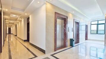 A hotel corridor with a marble floor, a wooden door, and a trash bin.