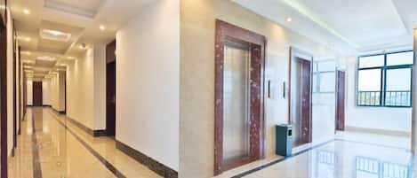 Un pasillo de hotel con piso de mármol, una puerta de madera y un bote de basura.