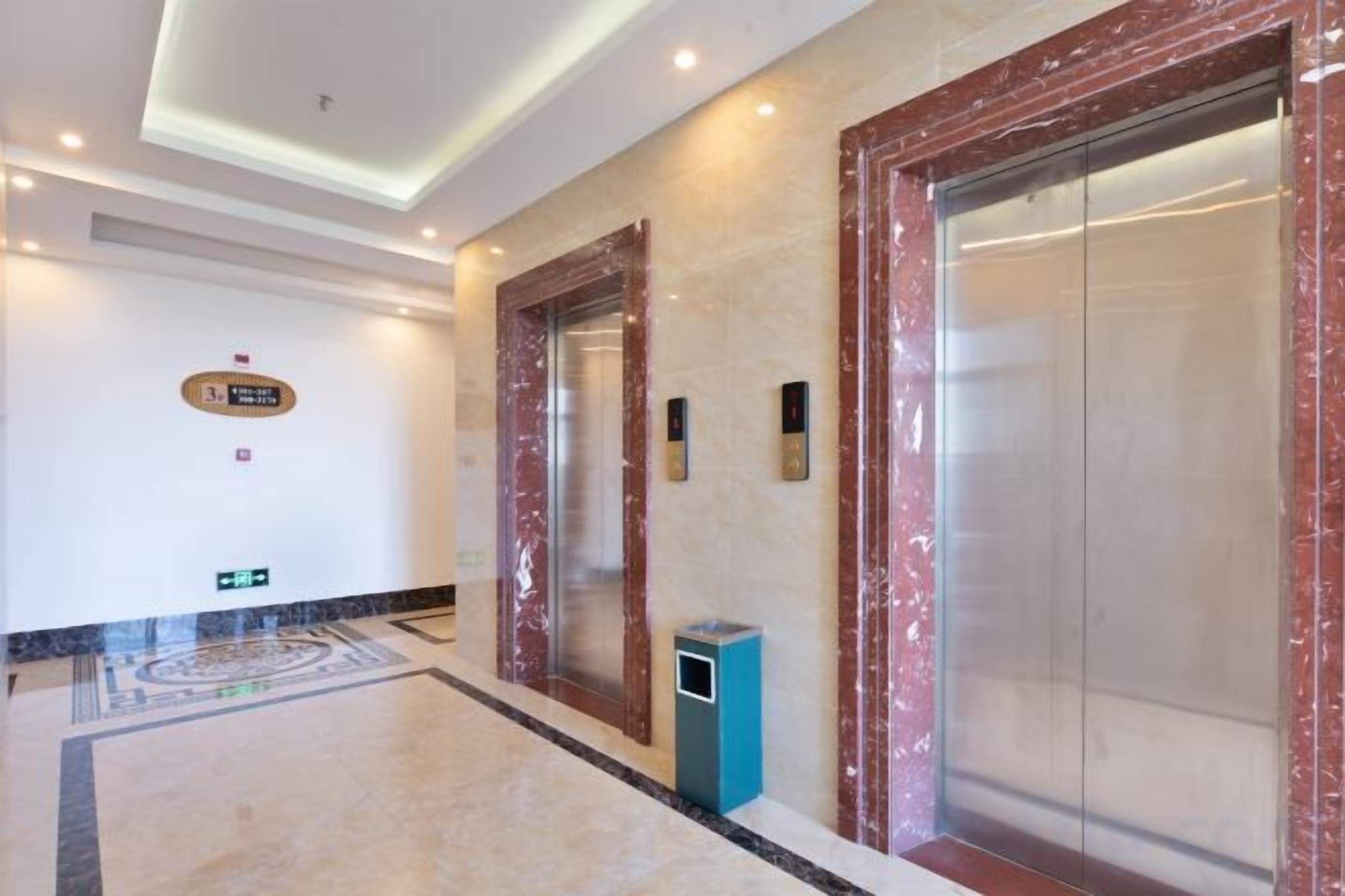 A hotel lobby with marble flooring, a reception desk, and two elevators.