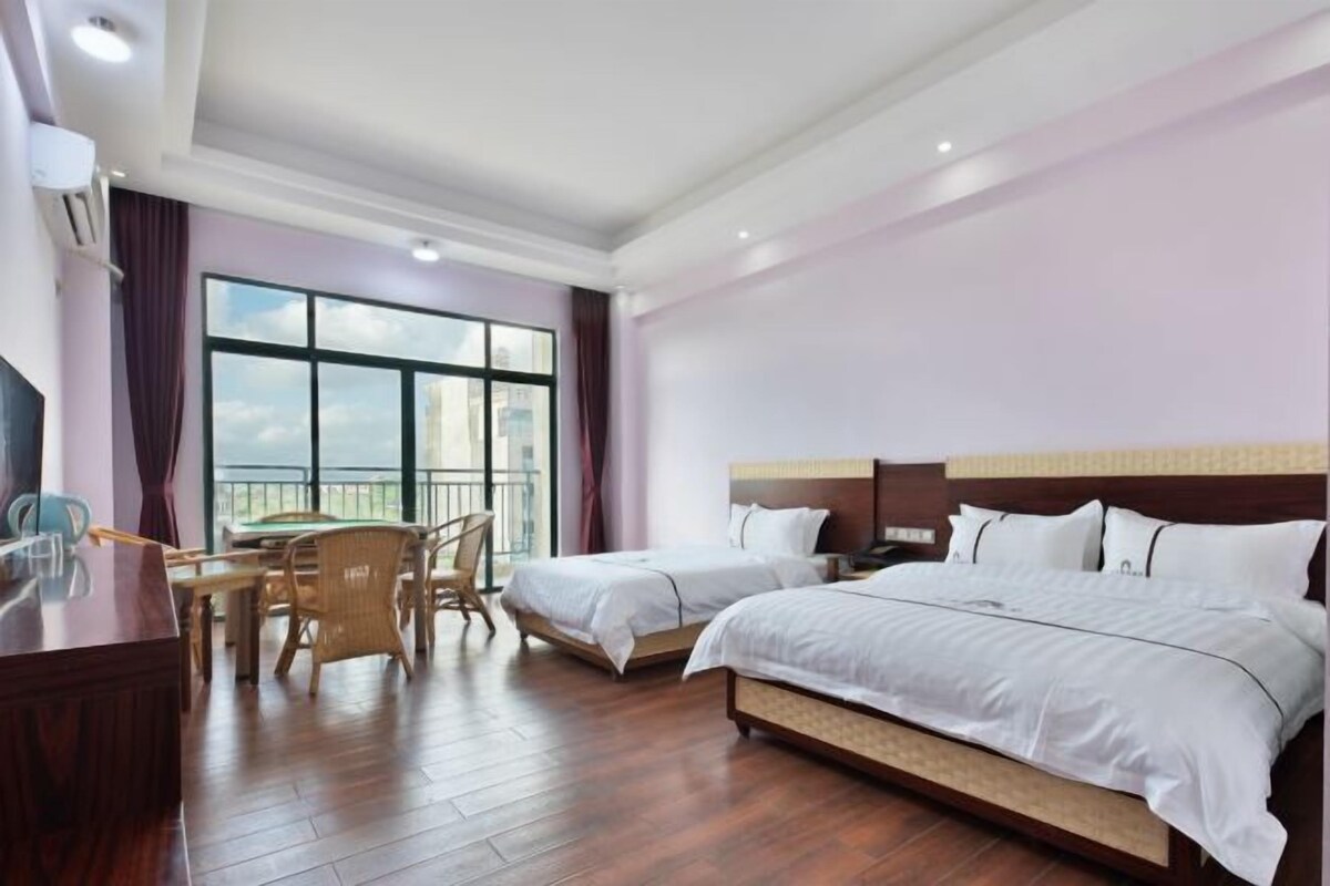Une chambre d’hôtel avec deux lits, un coin repas comprenant une table et des chaises, et une grande fenêtre donnant sur la ville.