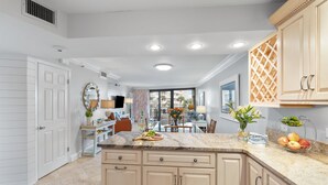 A modern kitchen with a marble countertop, beige cabinetry, and a dining area in the background. - CostaVista-Sandestin: Steps to Beach/Gulf Views! (Miramar Beach)