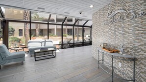 A spacious lobby with a modern design, featuring a seating area with sofas and a coffee table, a reception desk, and a large glass wall offering views of the outdoor area. - CostaVista-Sandestin: Steps to Beach/Gulf Views! (Miramar Beach)
