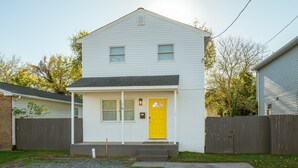 A two-story house with a yellow front door, a small porch, and a wooden fence. - Spacious 3BR in Phoebus - Great Monthly Rates (Hampton)
