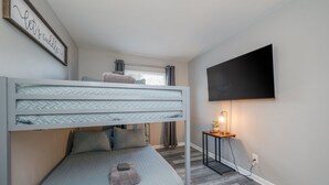 A bunk bed with a quilted mattress, a bedside table with a lamp, and a flat-screen TV mounted on the wall. - Spacious 3BR in Phoebus - Great Monthly Rates (Hampton)